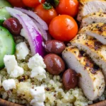 Close-up of a Mediterranean Quinoa Power Bowl with fluffy quinoa, grilled chicken breast, cherry tomatoes, crisp cucumber slices, Kalamata olives, red onion, and crumbled feta cheese, seasoned with black pepper and olive oil.