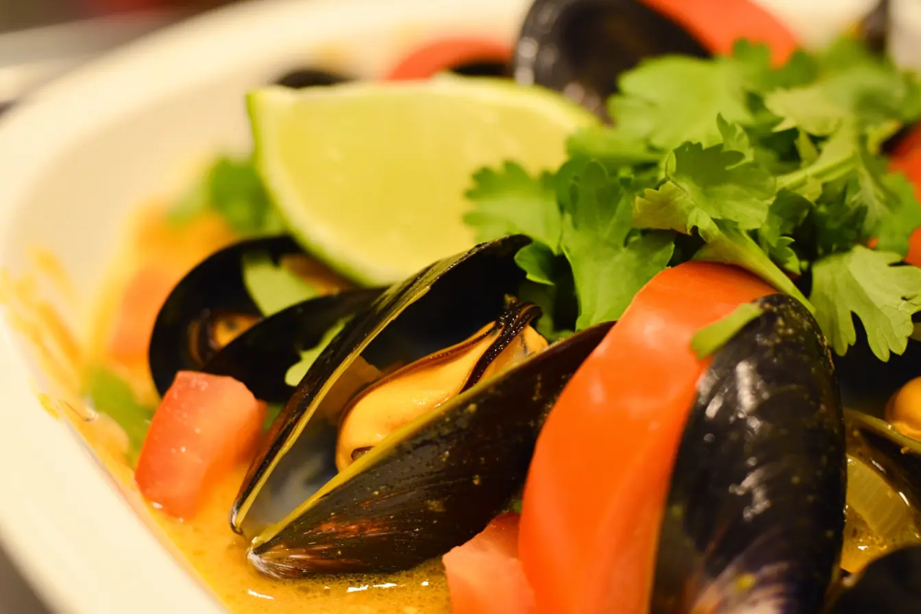Thai Mussels in Coconut Curry – A Rich & Flavorful Dish Close-up of Thai mussels in coconut curry, featuring plump mussels in a golden-yellow broth, garnished with fresh cilantro, red bell peppers, and a lime wedge.