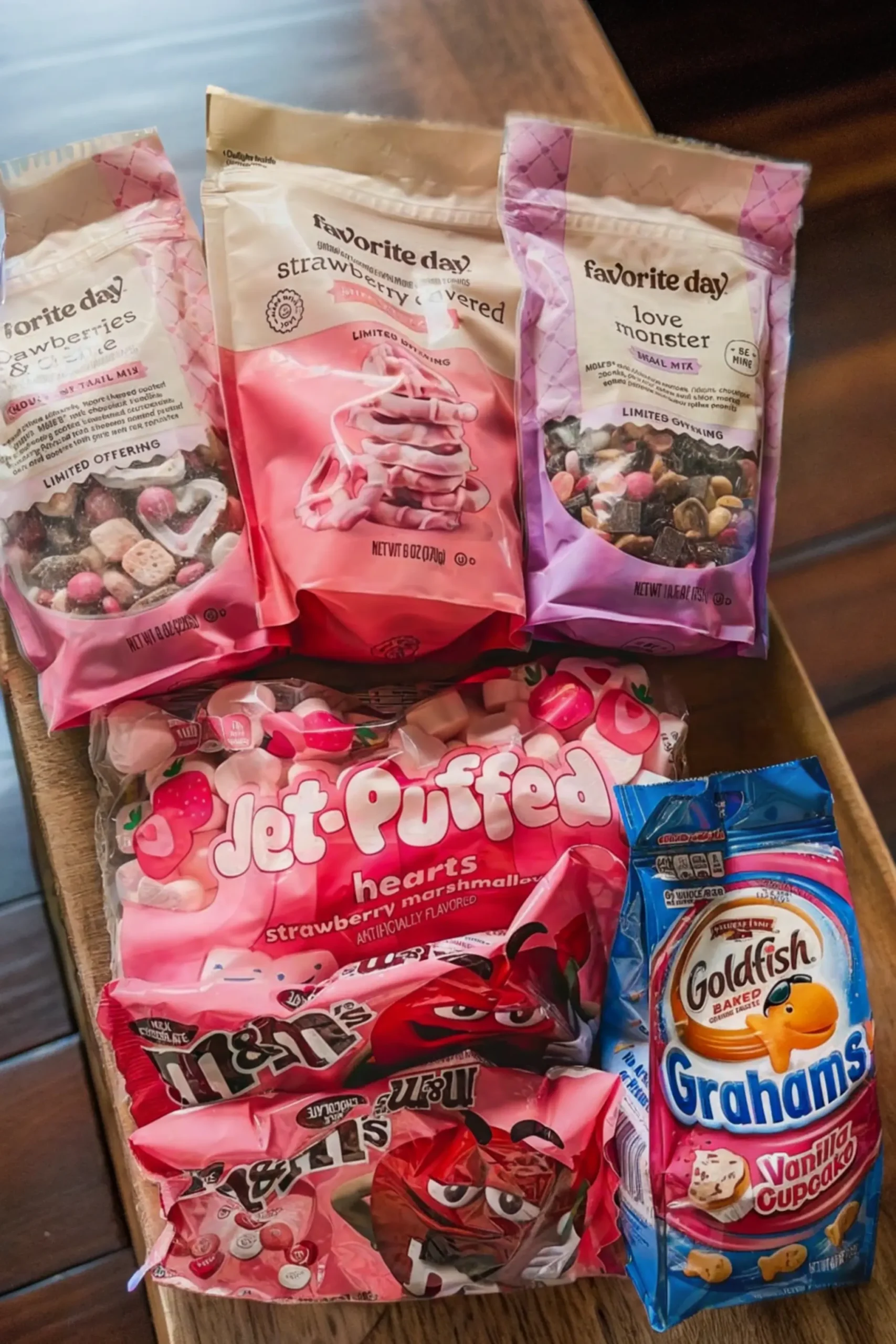 A selection of colorful ingredients for Cupid Crunch Valentine’s Day Trail Mix, including strawberry-covered pretzels, heart-shaped marshmallows, M&M’s, and vanilla graham crackers. 