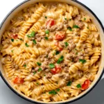 Creamy stovetop ground beef pasta in a white Dutch oven, garnished with fresh parsley and cherry tomatoes, placed on a white marble kitchen counter.