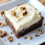 Keto banana bread brownie slice with creamy frosting and walnuts on a white plate