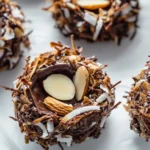 Close-up of no-bake chocolate nests made with toasted coconut flakes, almonds, and sugar-free dark chocolate, set on parchment paper. A crunchy, keto-friendly Easter treat with a rich, glossy chocolate coating.