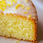 Close-up of a moist Lemon Almond Cake with a golden crust, topped with a glossy lemon glaze and fresh lemon zest.