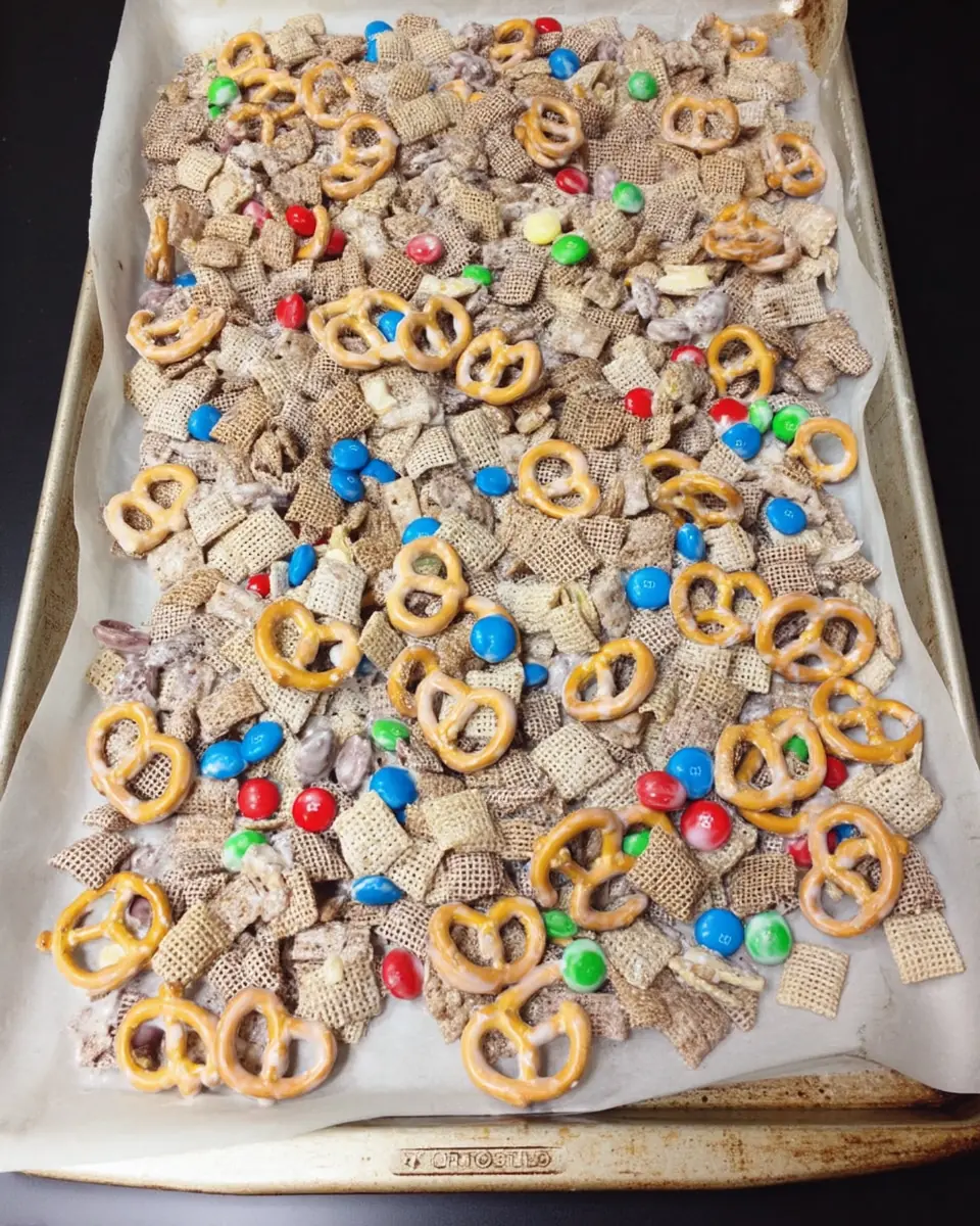 Patriotic snack mix with pretzels, cereal, chocolate candies, and white chocolate on a baking sheet lined with parchment paper.