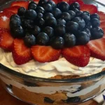 Close-up of a 4th of July trifle topped with fresh blueberries and sliced strawberries in a clear glass bowl with layered whipped cream and pound cake.