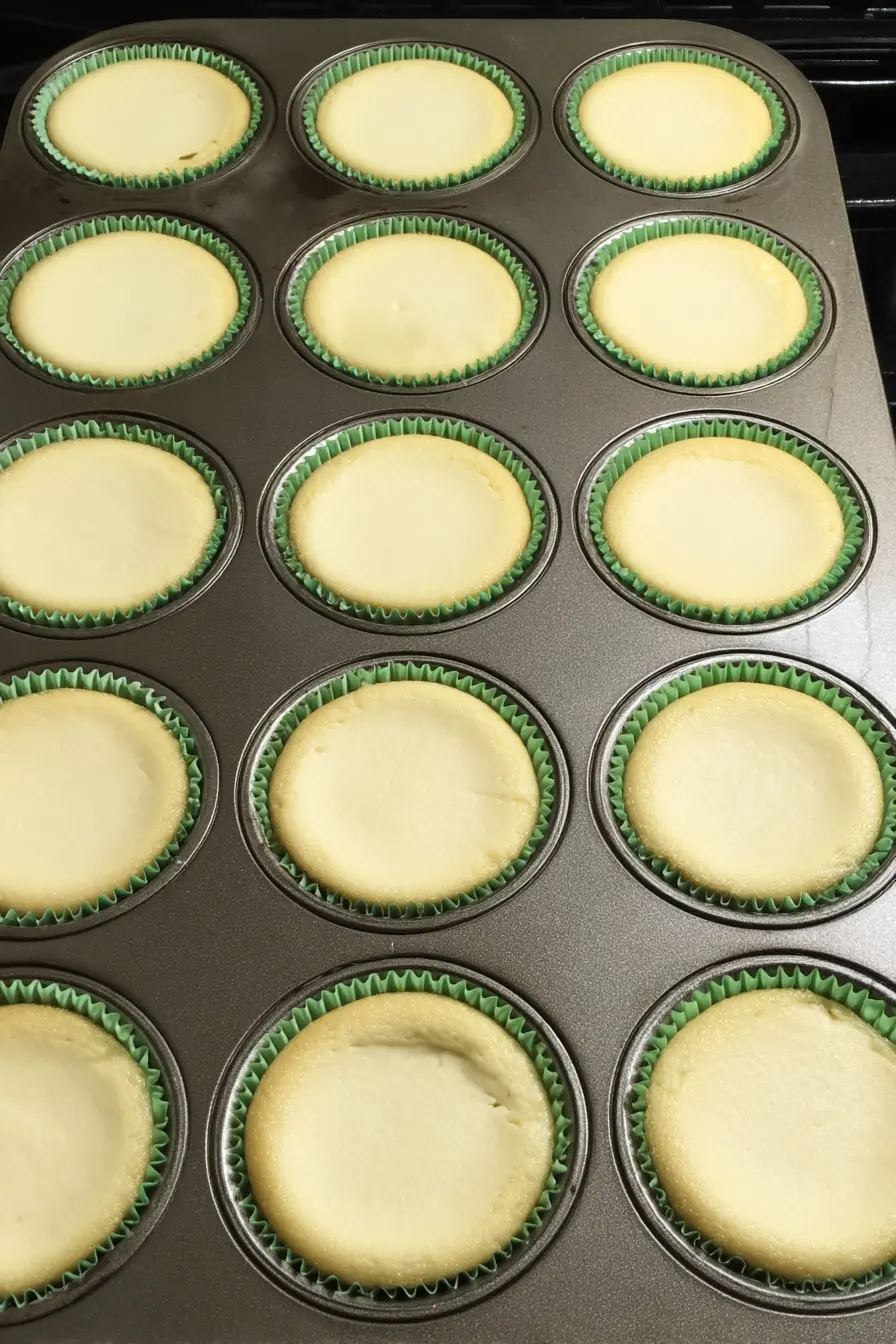Freshly baked mini cheesecakes in green liners cooling in a muffin tin