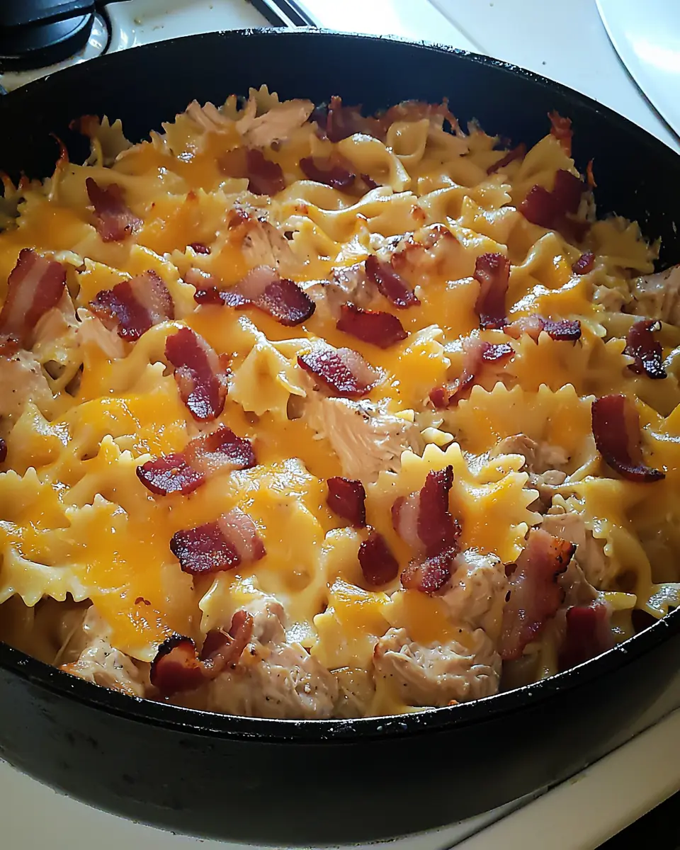 Chicken bacon ranch pasta bake with melted cheese and crispy bacon on top, served in a black skillet