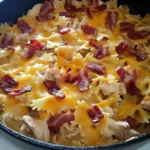 Creamy chicken bacon ranch pasta bake with melted cheese and crispy bacon in a cast iron skillet