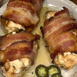 Bacon-wrapped jalapeño stuffed chicken breasts on a white plate with sliced jalapeños