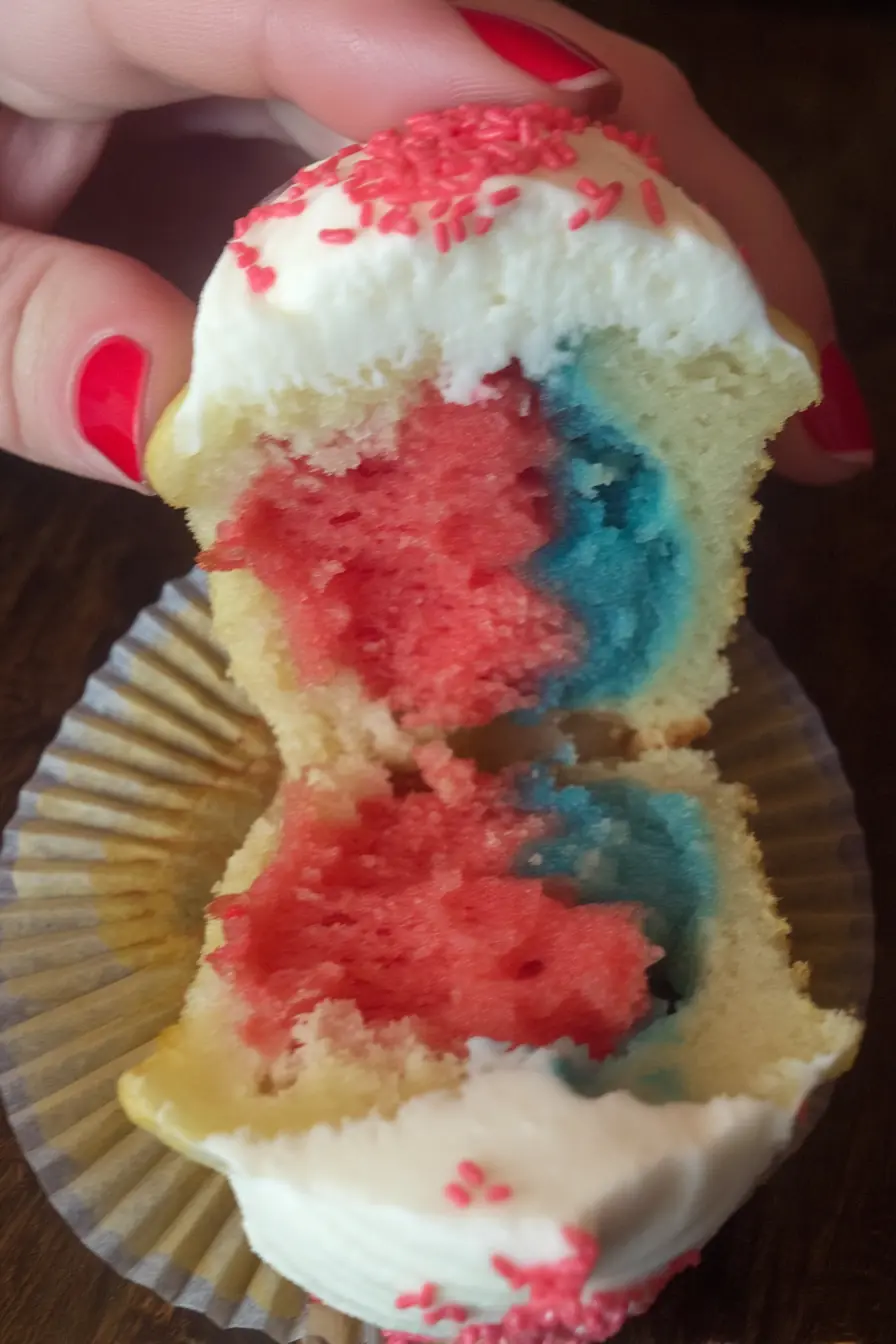 Split Fireworks Funfetti Cupcake with red, blue, and white layers and vanilla frosting topped with red sprinkles