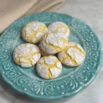 Close-up of lemon crinkle cookies stacked on a teal plate, dusted with powdered sugar
