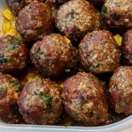 Oven baked Italian meatballs in sauce, freshly cooked and garnished with herbs in a serving container.