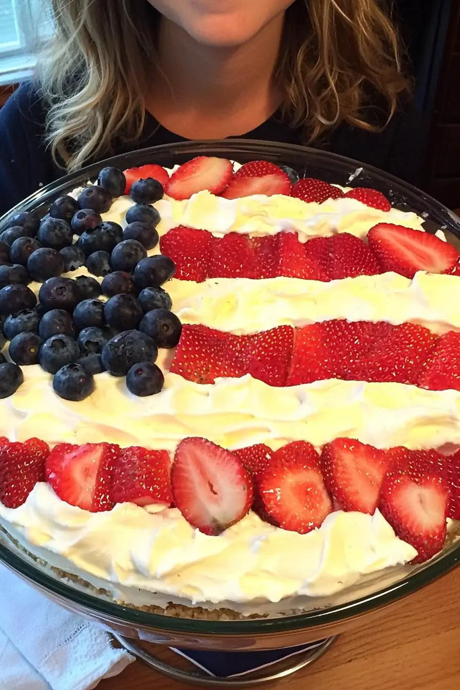 Patriotic 4th of July trifle topped with alternating rows of sliced strawberries, whipped cream, and a corner section of blueberries styled like the American flag.