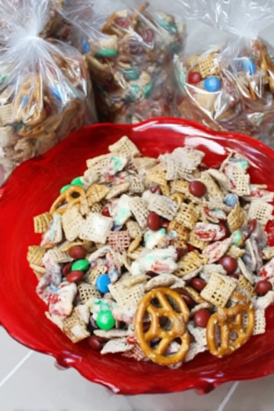 Patriotic snack mix in a red serving bowl with cereal, pretzels, and red, white, and blue chocolate candies, with gift bags filled in the background.
