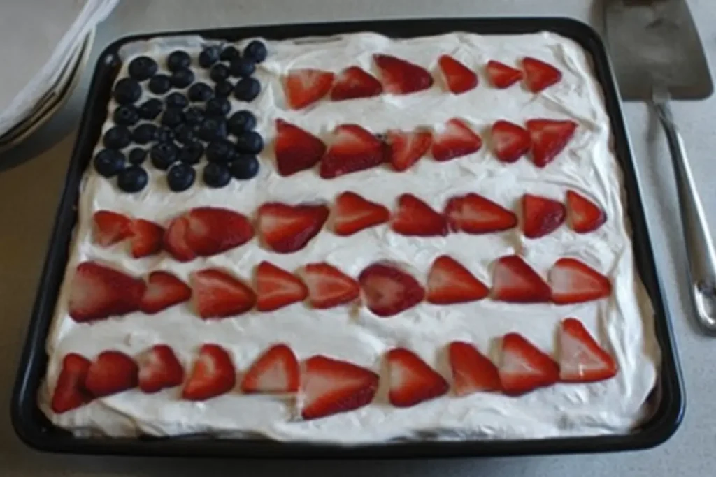 Patriotic Poke Cake topped with whipped cream, blueberries, and sliced strawberries in a flag design