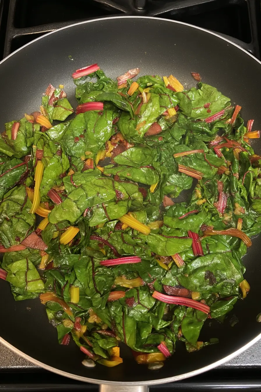 Rainbow chard leaves and stems sautéing in a skillet with olive oil and garlic