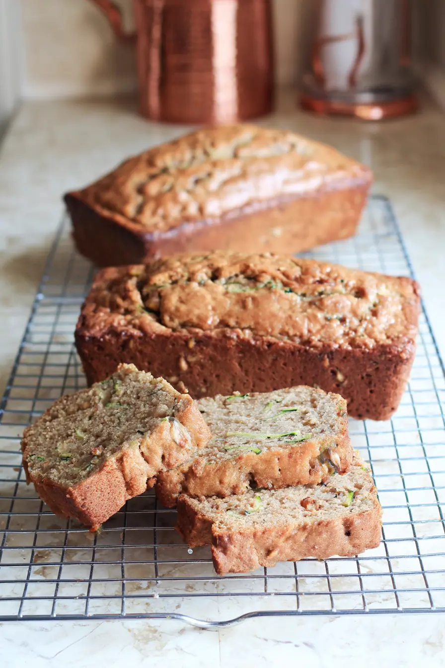 Sliced zucchini bread with applesauce on a wire rack, showing a moist crumb with visible zucchini and chopped nuts inside.