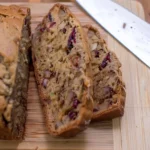 Sliced zucchini banana bread with cranberries and walnuts on a wooden cutting board