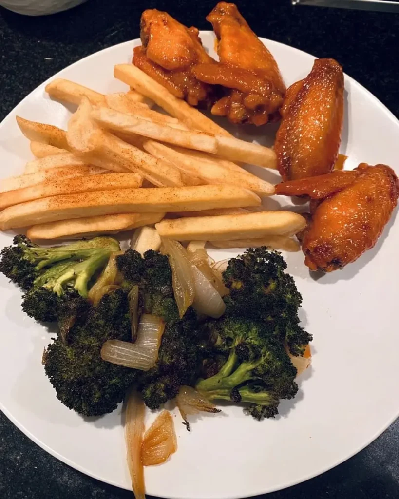 Plate with four crispy oven-baked hot wings, seasoned fries, and roasted broccoli-onion mix on a white dish
