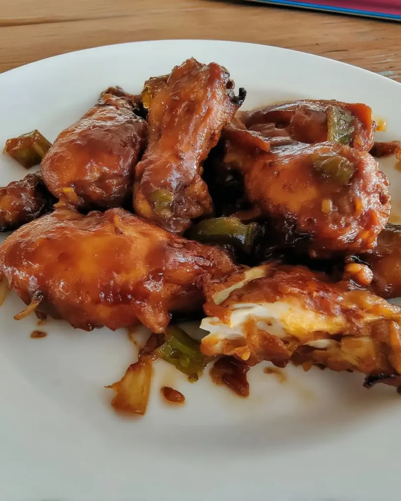 Sticky huli huli chicken wings coated in a pineapple-soy glaze, resting on a white plate with charred green onion pieces.