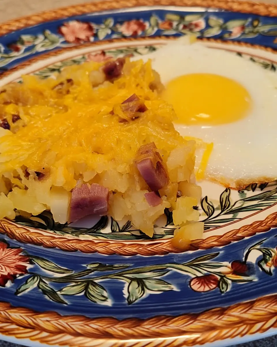 Cheesy ranch potatoes casserole with smoked sausage and melted cheddar next to a sunny-side-up egg on a blue floral plate.