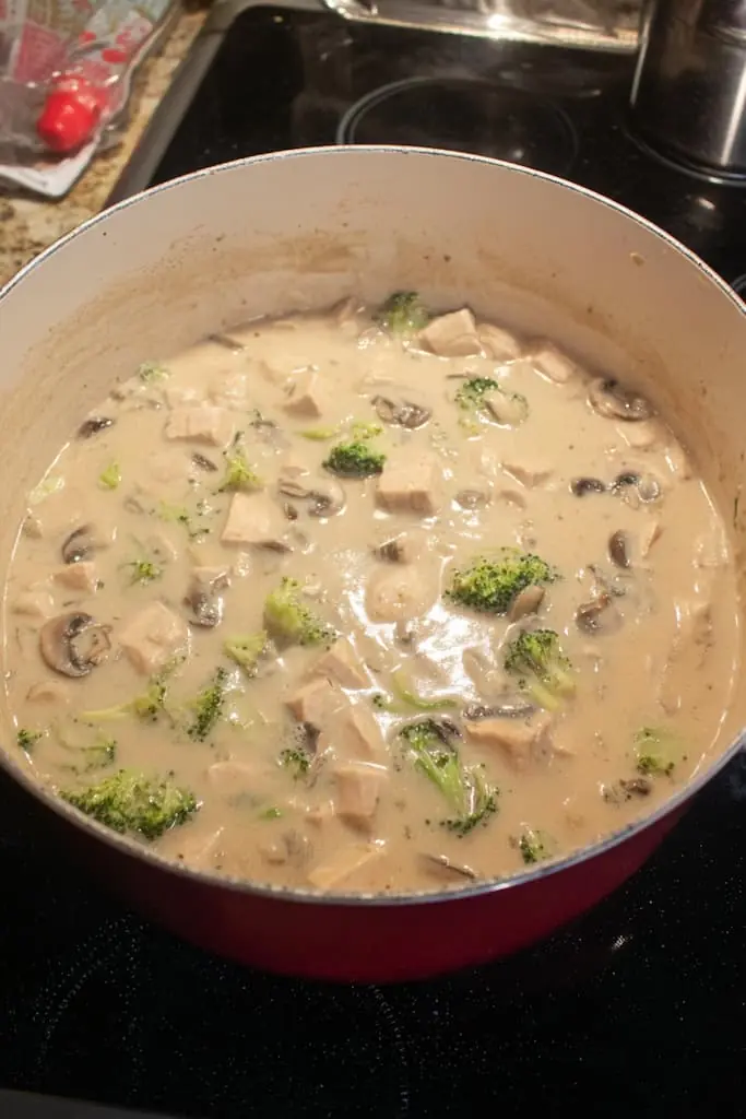 Creamy chicken and mushroom soup with broccoli florets simmering in a large pot on the stove