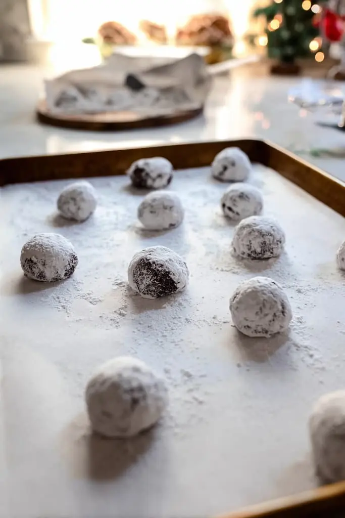 Cookie dough balls coated in powdered sugar on parchment-lined baking sheet ready to bake