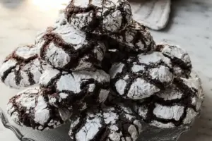 Stack of chocolate crinkle cookies with powdered sugar cracks on glass serving plate
