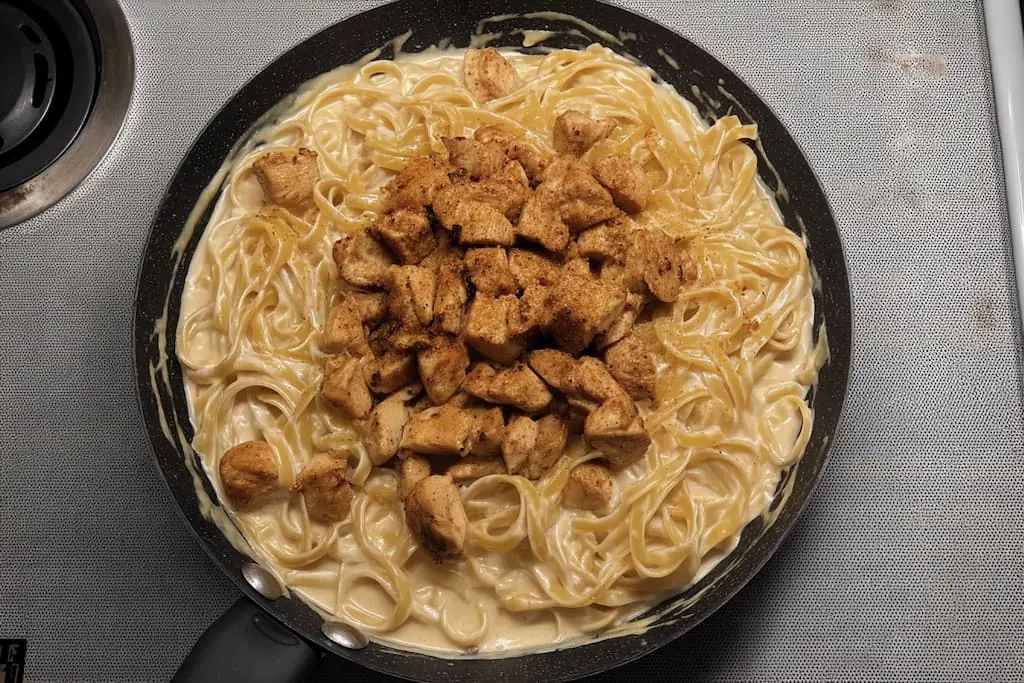 Overhead view of creamy cowboy butter chicken linguine with golden seasoned chicken pieces arranged on top of linguine pasta in a rich butter sauce, served in a black skillet