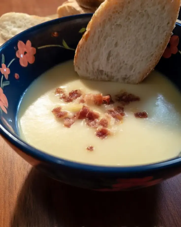 Bowl of creamy potato leek soup topped with crispy bacon pieces and served with crusty bread