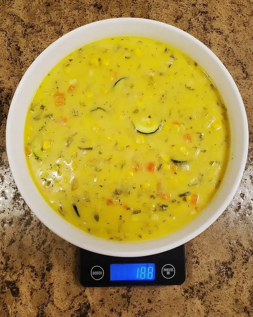Creamy yellow zucchini corn chowder in white bowl showing chunks of vegetables and herbs