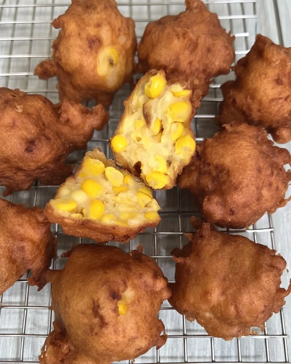 Crispy sweet corn fritters cooling on a wire rack, with two split open to show the tender corn-filled center.