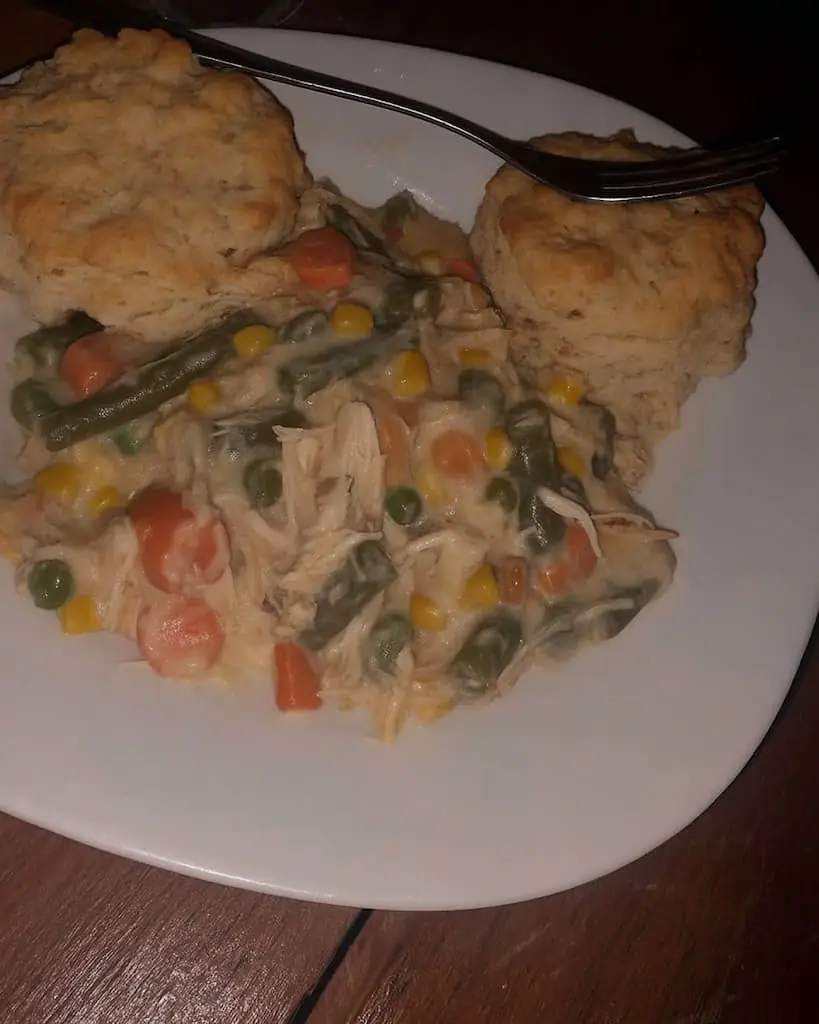 Plated serving of crockpot chicken pot pie featuring shredded chicken, carrots, peas, corn, green beans, and rich cream sauce, paired with two golden biscuits on a white plate.