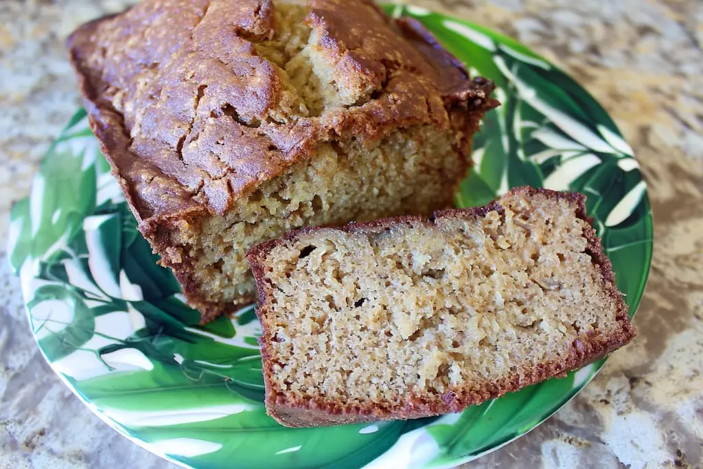 Golden brown banana bread loaf sliced on green tropical plate showing moist tender crumb