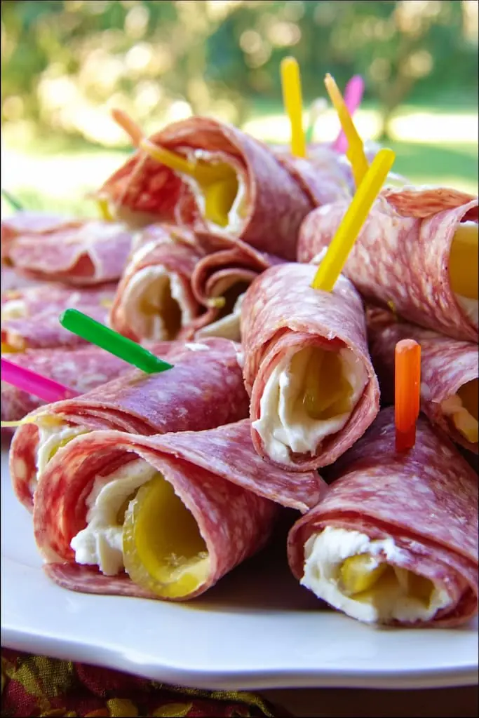 Easy keto salami roll-ups with cream cheese and pickles secured with colorful toothpicks on white plate