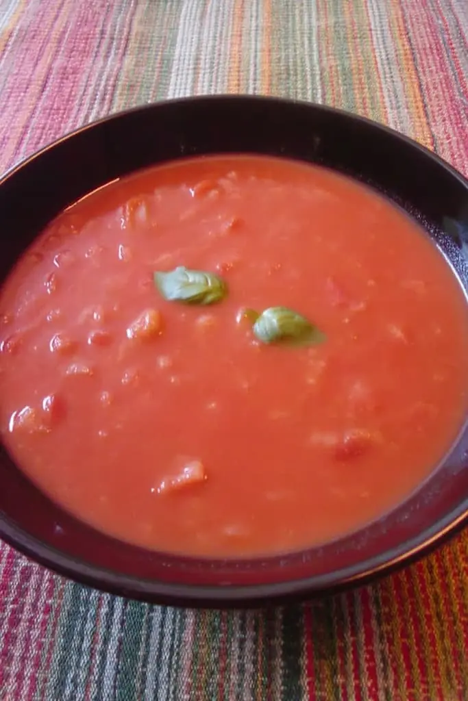 Smooth roasted tomato basil soup in a dark bowl with fresh basil garnish on a colorful striped placemat