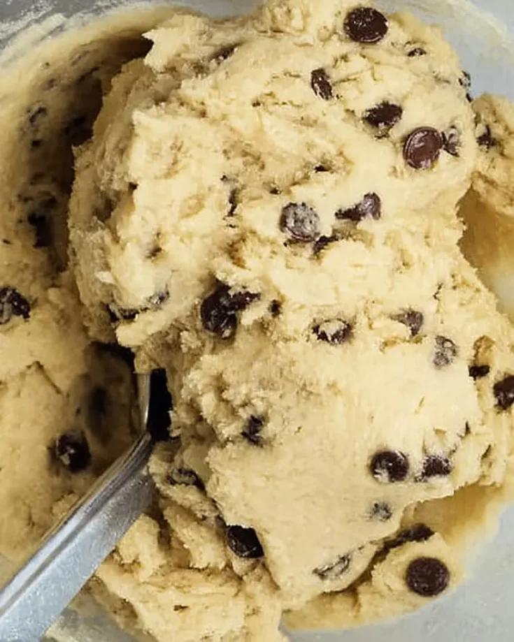 Creamy edible cookie dough loaded with chocolate chips in a glass bowl with a spoon