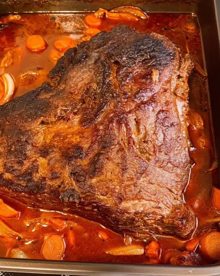 Tender French onion brisket in roasting pan with rich brown sauce and carrots after 3 hours of slow cooking