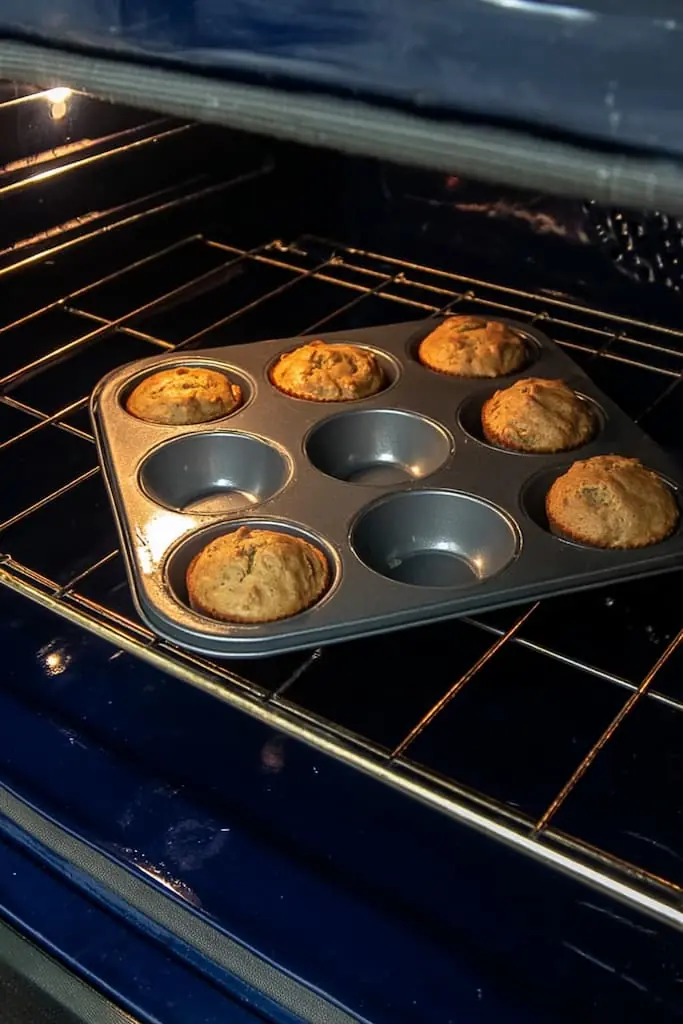 High protein muffins rising and browning in muffin tin inside oven, showing perfect golden color through oven door
