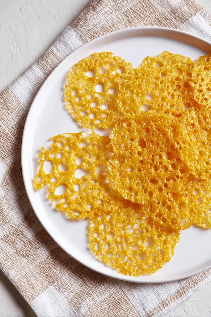 Golden keto cheese crisps with crispy lace texture on white plate with striped kitchen towel
