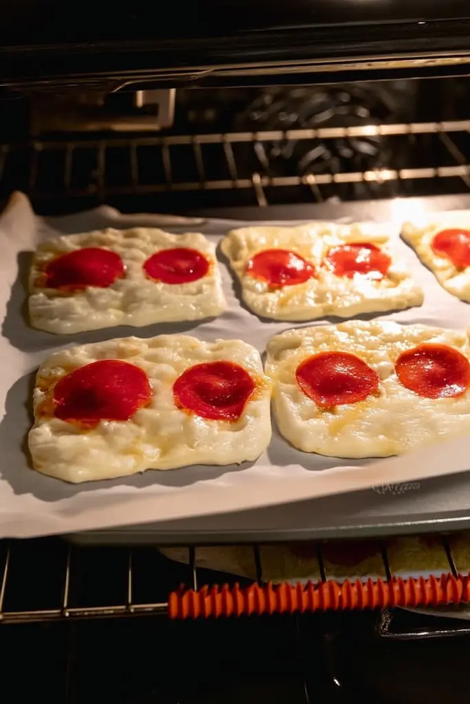Melted cheese and pepperoni keto pizza roll-ups bubbling in oven with golden edges