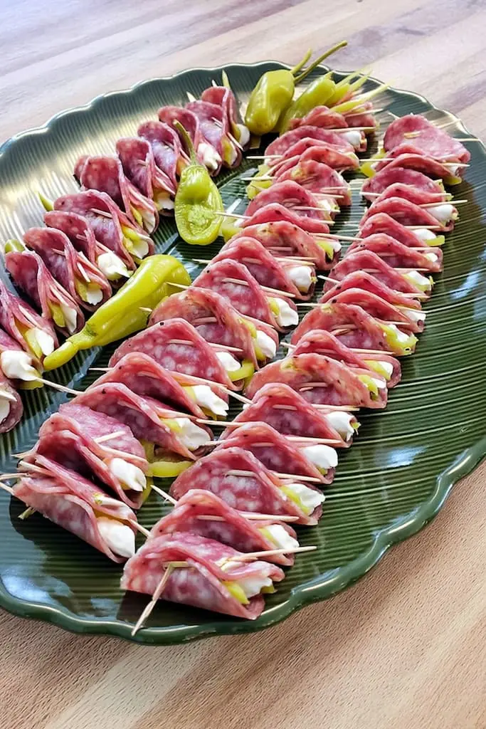 Large green glass platter filled with keto salami roll-ups with cream cheese and pepperoncini peppers arranged for party serving