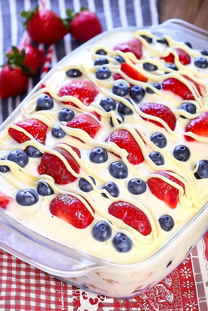 Finished no bake berry icebox cake in glass dish with white chocolate drizzle over fresh strawberries and blueberries, ready to serve