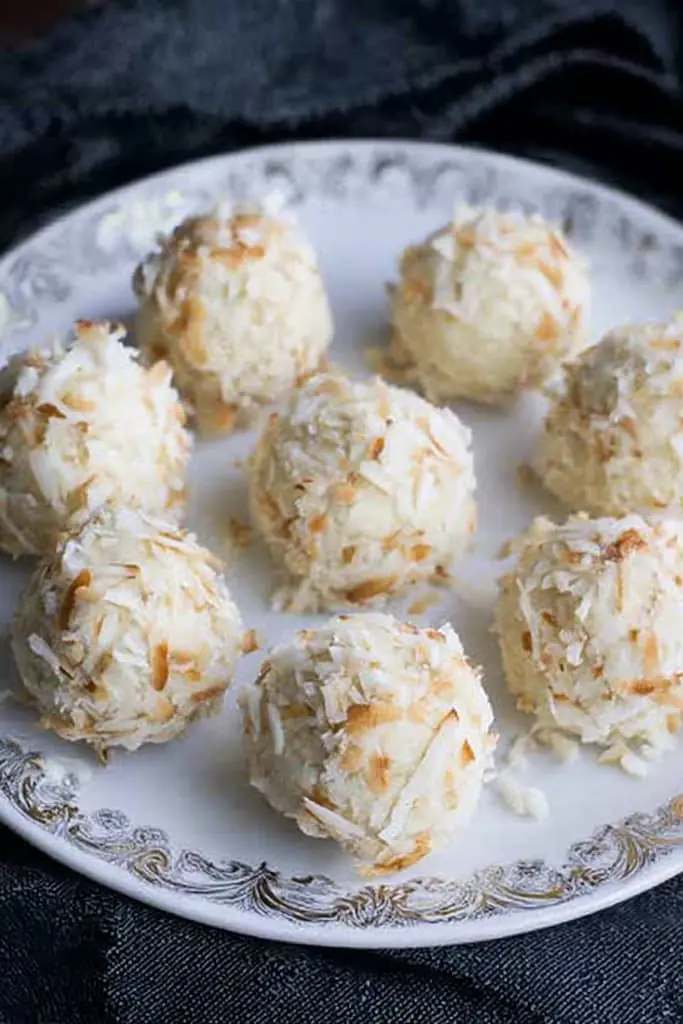 No-bake coconut fat bombs rolled in shredded coconut on decorative white plate