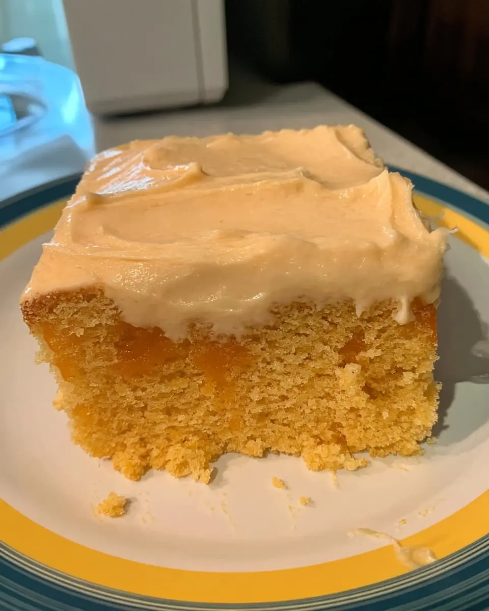 Square slice of orange creamsicle cake showing orange gelatin pockets and a thick layer of vanilla pudding whipped topping on a plate.