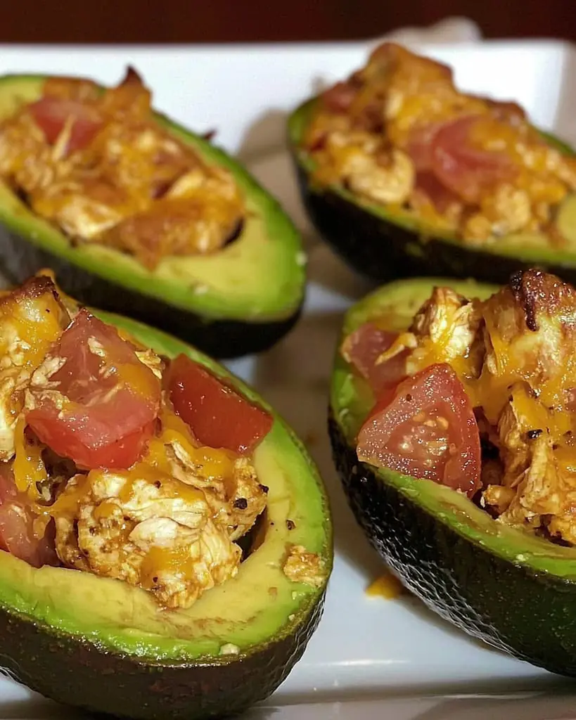 Oven-baked chicken avocado boats with melted cheddar cheese and taco seasoning on white plate