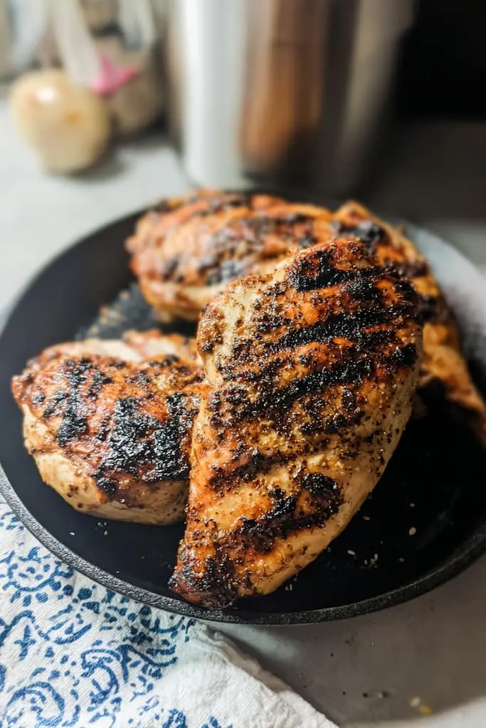 Perfectly grilled chicken breasts with golden brown skin and black char marks on a cast iron skillet, ready for slicing into Caesar wraps