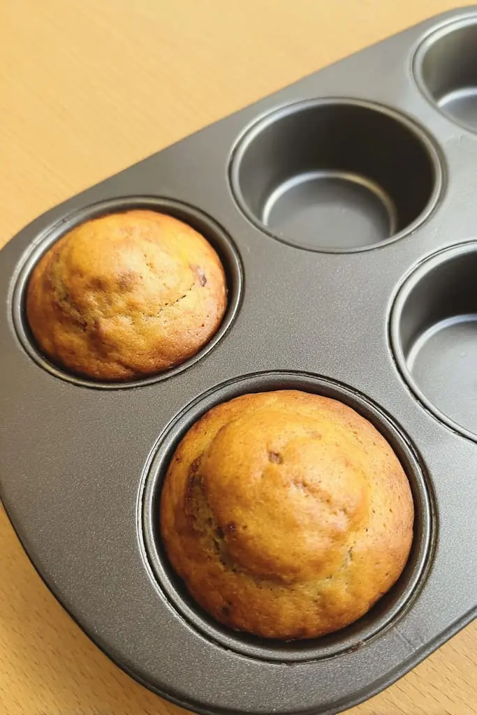 Two golden brown high protein muffins in nonstick muffin tin showing perfect dome tops and golden color