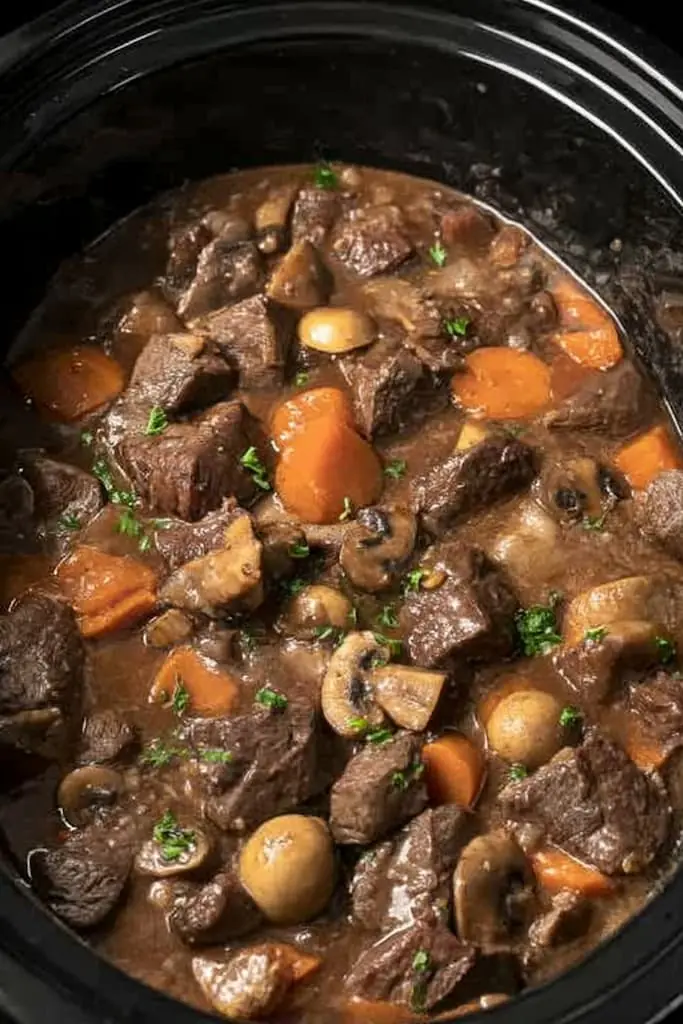 Slow cooker beef bourguignon with tender beef chunks, pearl onions, mushrooms and carrots in rich wine sauce, garnished with fresh parsley