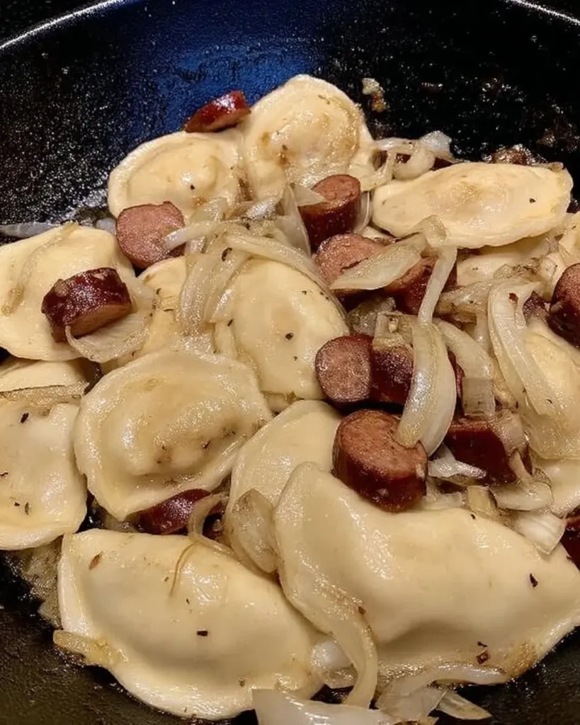 Pierogies, sliced kielbasa, and caramelized onions sizzling together in a cast-iron skillet.